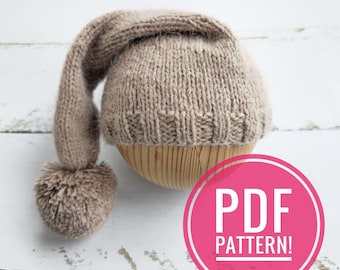 Könnte beinhalten: Eine gestrickte Baby-Mütze mit einem langen, schlaffen Rand und einem Bommel am Ende. Die Mütze ist hellbraun und wird auf einer Holzform präsentiert. Der Text "PDF PATTERN!" befindet sich auf einem rosa Kreis.