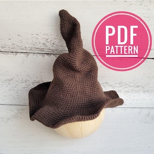 Può includere: Cappello da strega in crochet marrone con una cima a punta, esposto su un supporto in legno. Il cappello è un modello PDF.