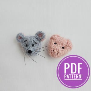 May include: Two handmade, knitted animal heads: a gray mouse with whiskers and a pink pig. The mouse has large ears and a black nose. The pig has small black eyes and a snout. A purple circle with the text "PDF PATTERN!" is in the lower right corner.