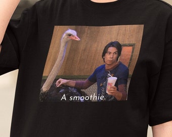 Puede incluir: Camiseta negra con un gráfico de un hombre sosteniendo un batido y una avestruz. El texto "A smoothie." está impreso debajo del gráfico.