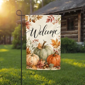 May include: A rectangular garden flag featuring the word Welcome in black cursive script. The design includes three pumpkins in shades of orange, light green, and cream, surrounded by watercolor illustrations of autumn leaves, acorns, and berries.
