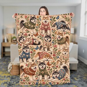 May include: A rectangular throw blanket featuring a repeating pattern of Shiba Inu dogs wearing colorful knit sweaters with floral designs, interspersed with various flowers, leaves, and butterflies on a light beige background.