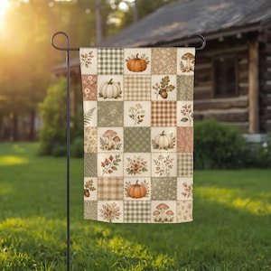 May include: A rectangular garden flag featuring a patchwork design of squares with various autumn-themed illustrations including orange and white pumpkins, mushrooms, acorns, berries, and floral sprigs, interspersed with green and brown plaid patterns.