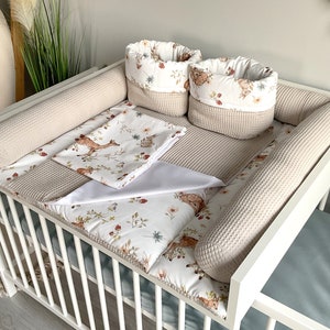 Könnte beinhalten: Ein weißes Babybett mit einem beige-weißen gemusterten Bettumrandung, einem beige-weißen gemusterten Bettlaken und zwei beige-weißen gemusterten Aufbewahrungskörben. Das Babybett ist mit einem beige-weißen gemusterten Bettlaken und einem beige-weißen gemusterten Bettumrandung dekoriert.