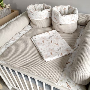 Peut inclure: Un lit bébé blanc avec un matelas à langer en tissu gaufré beige et un ensemble de pare-chocs de lit à motifs beige et blanc. Le matelas à langer est doté d'un drap assorti à motifs beige et blanc et d'un petit panier à motifs beige et blanc.