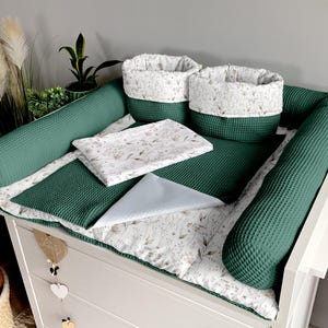 Peut inclure: Un ensemble de table à langer pour bébé avec un matelas à langer vert gaufré, deux boudins assortis et deux paniers de rangement. L'ensemble comprend une housse de matelas à langer et un petit lange bleu clair. Les paniers et la housse présentent un motif floral.