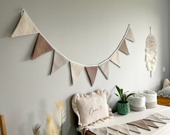 May include: A white and brown fabric bunting with the name "Emma" embroidered on a white pillow. The bunting is hanging on a white wall with a dreamcatcher and a potted plant on a white dresser.