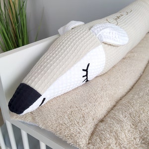 Op de afbeelding: Een witte en beige babybedbumper met een wit en zwart dierengezichtontwerp. De bumper is gemaakt van zacht, pluche stof en heeft een wafelstructuur. Het dierengezicht heeft een zwarte neus en ogen.