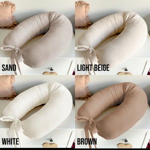 May include: Four waffle-textured pregnancy pillows in different colors: sand, light beige, white, and brown. Each pillow has a tied ribbon at the end.