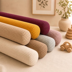Puede incluir: Una colección de seis cojines cilíndricos con una textura de tejido de gofre. Los cojines están dispuestos en una formación apilada y vienen en una variedad de colores que incluyen burdeos intenso, amarillo mostaza, beige, canela, gris y rosa.