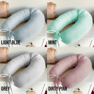 May include: Four donut-shaped pillows in different colors: light blue, mint green, gray, and dusty pink. The pillows are made of a waffle-textured fabric and have a tied ribbon at the opening.