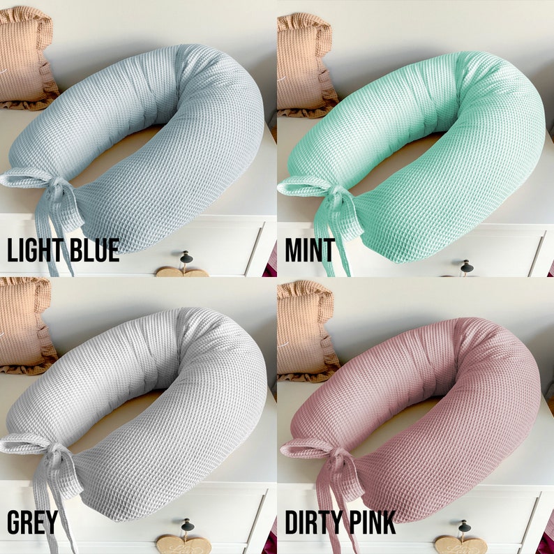 May include: Four donut-shaped pillows in different colors: light blue, mint green, gray, and dusty pink. The pillows are made of a waffle-textured fabric and have a tied ribbon at the opening.