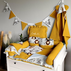 Peut inclure: Un ensemble de chambre d'enfant avec une table à langer blanche, comprenant une literie jaune en nid d'abeille et des accessoires imprimés d'animaux de safari. Comprend une couverture, des oreillers et des paniers de rangement. Une bannière avec des drapeaux éléphants et triangulaires est suspendue au-dessus.