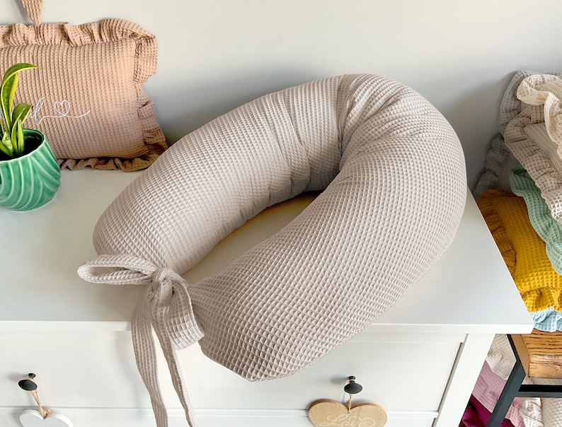 May include: A beige waffle-textured donut-shaped pillow with a matching fabric tie. The pillow is on a white dresser.