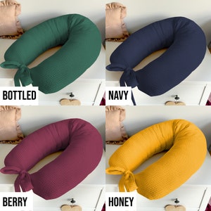 May include: Four different colored waffle-textured donut pillows with a bow tie. The colors are bottled green, navy blue, berry red, and honey yellow. The pillows are arranged in a grid pattern on a white surface.