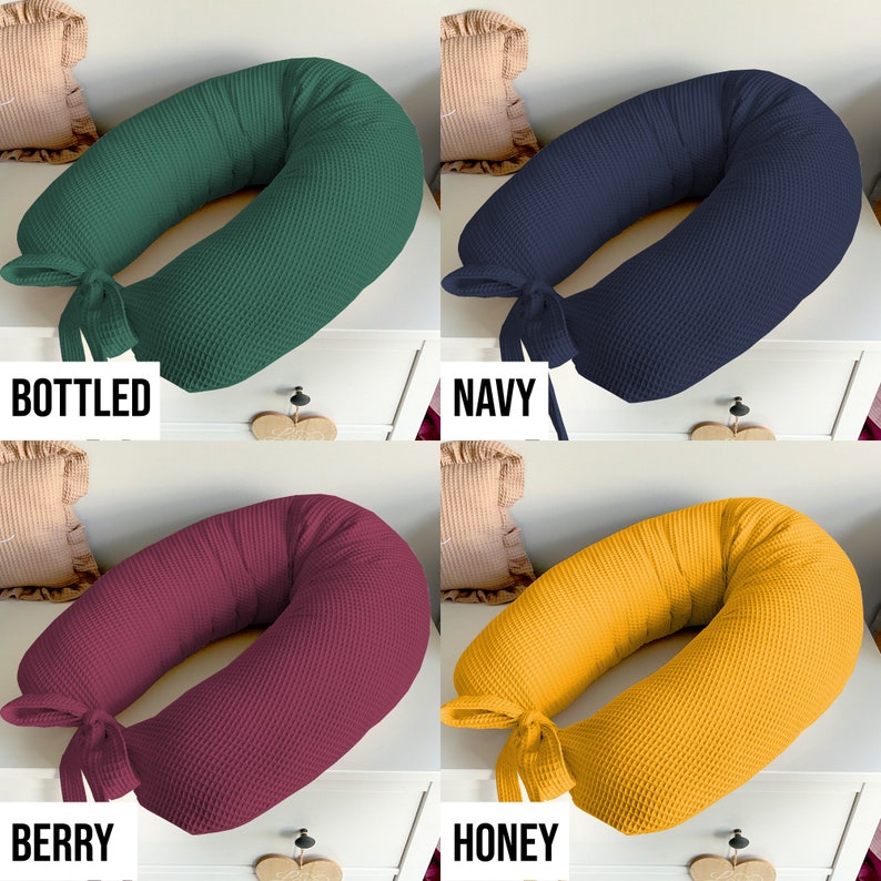 May include: Four different colored waffle-textured donut pillows with a bow tie. The colors are bottled green, navy blue, berry red, and honey yellow. The pillows are arranged in a grid pattern on a white surface.