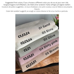 May include: A stack of five folded knitted blankets in various colours labelled 01 Sand, 02 Ecru, 03 Olive, 04 Dirty pink, and 05 Brown. Each blanket features a textured waffle-knit pattern and includes printed text codes C2, C3, C4, or C1.
