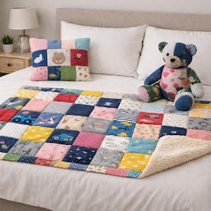 Op de afbeelding: Een patchworkdeken met een teddybeer en een bijpassend kussen op een bed. De deken heeft vierkanten in verschillende kleuren en patronen, waaronder auto's, dieren en bloemmotieven. De teddybeer is blauw en wit.