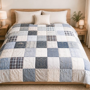 Könnte beinhalten: Eine Patchwork-Tagesdecke mit einem Raster aus quadratischen Stoffbahnen in verschiedenen Blau-, Weiß- und Grautönen. Das Design umfasst denimartige Taschen, Hemdenstoff und Karomuster, die in einem sich wiederholenden Schachbrettmuster angeordnet sind.