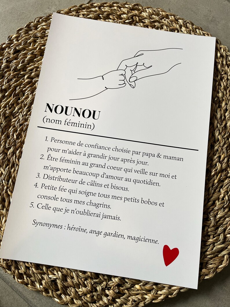 May include: A black and white line drawing of two hands holding pinkies, with the word "NOUNOU" (meaning "nanny" in English) written in black text below the drawing. The text defines the word "NOUNOU" as a person of trust chosen by parents to help a child grow, a caring and supportive person, a giver of hugs and kisses, a comforter of hurts and sorrows, and someone who will always be remembered. The text ends with the word "magicienne" (meaning "magician" in English) and a red heart.