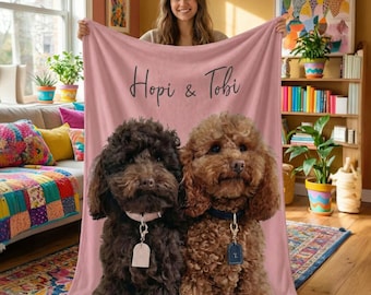 May include: A soft, light pink fleece blanket featuring a custom print of two curly-haired dogs, one dark brown and one light brown, each wearing a collar with a tag. The text "Hopi & Tobi" is printed in a dark script font above the dogs.
