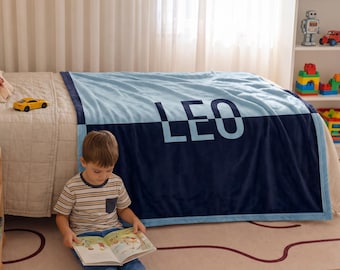 May include: A soft, rectangular fleece blanket featuring a two-tone design with a light blue top half and a dark navy blue bottom half. The name LEO is printed in large, bold, light blue capital letters across the center of the blanket.