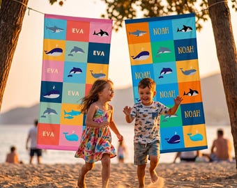 May include: Two rectangular beach towels hanging on a line. The left towel features a pink and blue grid pattern with whale and dolphin illustrations and the name EVA. The right towel has an orange and blue grid with similar sea life and the name NOAH.