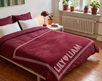 May include: A deep burgundy duvet cover featuring a white rectangular border and the text LILY HEART LIAM printed in a bold, linear font. The bedding set includes matching burgundy pillowcases and white pillows, displayed on a wooden bed frame.
