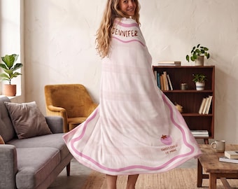 May include: A white blanket featuring a light pink plaid pattern, a wavy pink border, and the name JENNIFER printed in brown. The blanket also displays a small pink strawberry graphic and the text SWEET CHILD OF MINE in brown lettering.