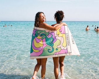 May include: A rectangular beach towel featuring a colorful graphic design with swirling patterns in shades of purple, yellow, and teal. The towel includes the text AQUARIUS and AMELIA printed in black capital letters on a white background border.