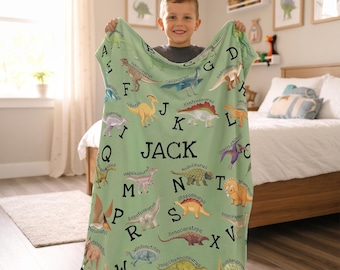 May include: A light green fleece blanket featuring a dinosaur alphabet print with various colorful dinosaur illustrations, their names, and the name JACK printed in large black letters in the center of the fabric.