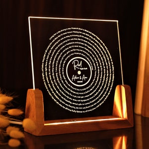 May include: A wooden stand with a clear acrylic panel displaying a circular design of song lyrics. The lyrics are in a white font and the centre of the design features a record with the text "Red River Blue" and "Adam & Ava" in a gold font.