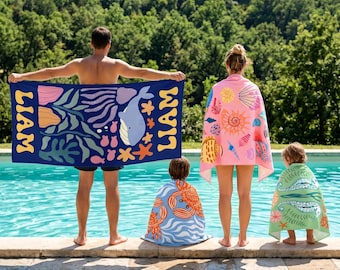 May include: A rectangular dark blue beach towel with the name LIAM printed in yellow, featuring a whale, starfish, and seaweed pattern. A pink towel with seashell prints, a light blue towel with orange crab prints, and a green towel with sea life.