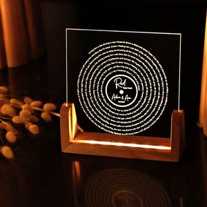 May include: A wooden stand with a clear acrylic plaque featuring a circular design with a record-like spiral pattern. The plaque has the text "R.M. After A" in white lettering.