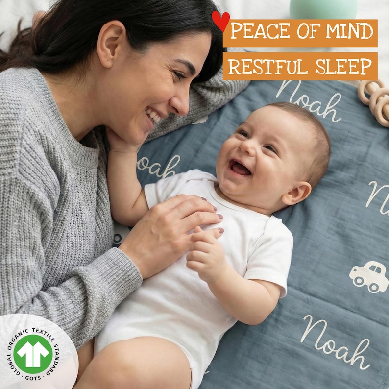 A smiling woman lies on a blue blanket with a baby named Noah, both appearing happy and content.