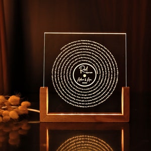 May include: A wooden frame with a clear acrylic panel displaying a record-shaped design with a song lyric etched in a spiral pattern. The centre of the record features a smaller circle with the text "Red" and "Adam & Amy" in a handwritten font.