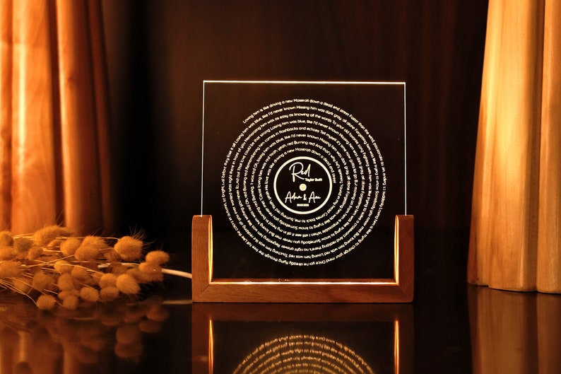 May include: A wooden frame with a clear acrylic panel displaying a record-shaped design with a song lyric etched in a spiral pattern. The centre of the record features a smaller circle with the text "Red" and "Adam & Amy" in a handwritten font.