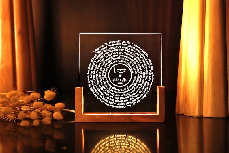 May include: A wooden stand with a clear acrylic panel displaying a circular design with the words "Whenever I'm alone with you You make me feel om home again" and "Love song Adam & Amy".