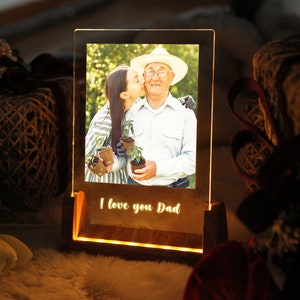 Puede incluir: Un marco de fotos iluminado con una foto de una persona besando a una persona mayor. La base del marco tiene las palabras "I love you Dad" iluminadas. El marco es de madera y tiene un brillo c&aacute;lido.