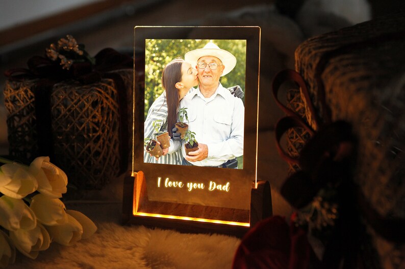 Puede incluir: Un marco de fotos iluminado con una foto de una persona besando a una persona mayor. La base del marco tiene las palabras "I love you Dad" iluminadas. El marco es de madera y tiene un brillo c&aacute;lido.