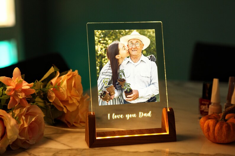 Puede incluir: Un marco de fotos iluminado con una foto de una mujer besando a un hombre mayor. El marco es de acr&iacute;lico transparente y se apoya en una base de madera. Las palabras "I love you Dad" est&aacute;n iluminadas en la parte inferior.