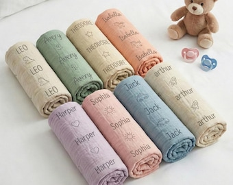 May include: Eight rolled muslin swaddle blankets in various pastel colors, each personalized with a name and a small icon. The names include Leo, Avery, Theodore, Isabella, Harper, Sophia, Jack, and Arthur. A brown teddy bear and two pacifiers are nearby.