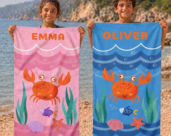 May include: Two rectangular beach towels featuring a cartoon crab, seaweed, a small fish, and a seashell. The pink towel displays the name EMMA, while the blue towel displays the name OLIVER. Both towels have a wavy water pattern at the top.