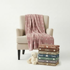 May include: A stack of personalized baby blankets in various colors, each with a name embroidered on it. A matching blanket is draped over a beige armchair. A teddy bear sits in front of the blankets.