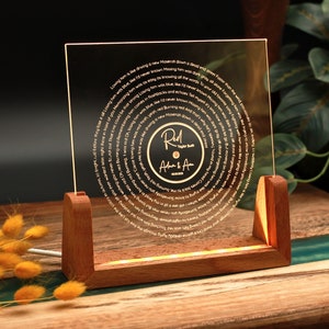 May include: A clear acrylic record with a gold inscription of song lyrics in a spiral pattern. The record is on a wooden stand with a light shining through the acrylic. The record has a gold label with the text "Red" and "Adam & Ava" in cursive.