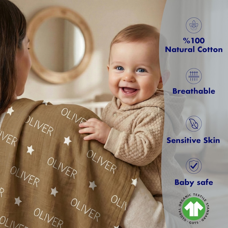 A smiling baby wearing a brown blanket with the name "OLIVER" printed on it, being held by a woman.