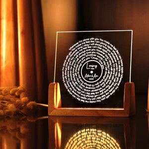 May include: A clear acrylic record-shaped plaque with a white inscription that reads "Whenever I'm alone with you You make me feel like I am young again" and "I will always love you However long we stay I will always love you Whatever words I say I will always love you However far away I will always love you Cause I will always love you." The plaque is on a wooden stand and has the words "Longing After & After" in the centre.