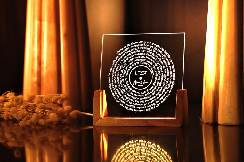 May include: A clear acrylic record-shaped plaque with a white inscription that reads "Whenever I'm alone with you You make me feel like I am young again" and "I will always love you However long we stay I will always love you Whatever words I say I will always love you However far away I will always love you Cause I will always love you." The plaque is on a wooden stand and has the words "Longing After & After" in the centre.