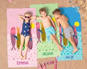 May include: Three rectangular beach towels in pink, light green, and blue, each featuring a repeating fish pattern and a personalized name printed at the bottom: EMMA on the pink towel, NOAH on the green towel, and JACK on the blue towel.