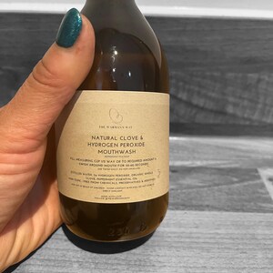 Op de afbeelding: Een bruine glazen fles met een etiket waarop "The Warmann Way Natural Clove & Hydrogen Peroxide Mouthwash" staat. Het etiket bevat ook gebruiksaanwijzingen, ingredi&euml;nten en waarschuwingen. De fles is 230 ml.